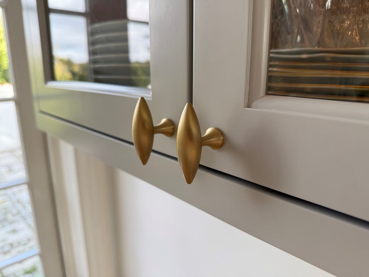 Nærbillede af to ovale Nyholm-knopper i messing på en vitrine