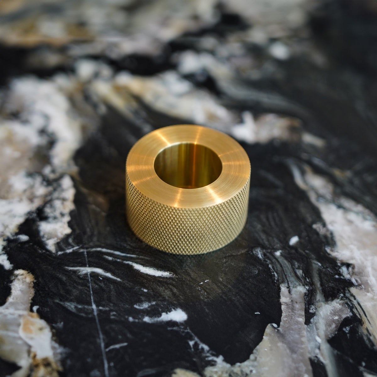 Ringformet Kastellet-greb i messing med diamond cut på en mørk stenflade.