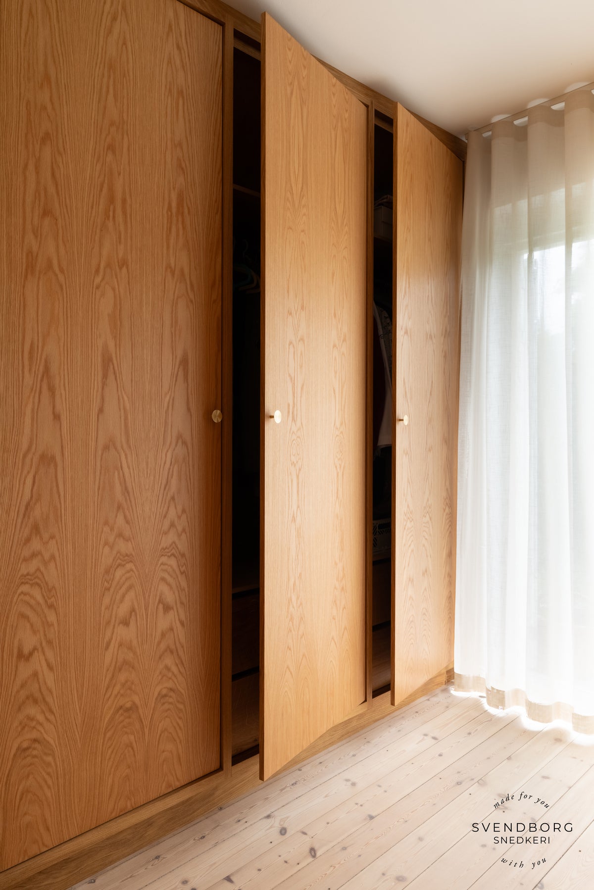 Trægarderobe med delvist åbne døre og runde København-knopper i messing.