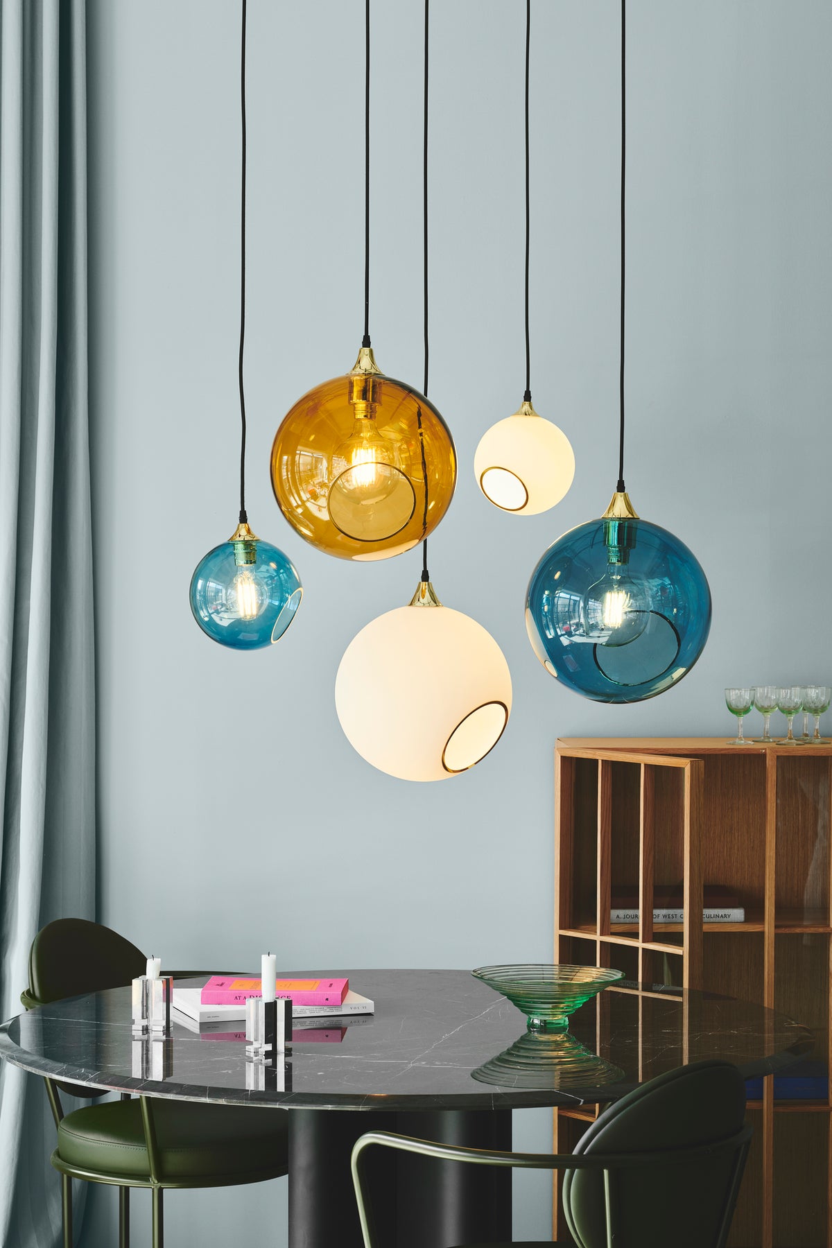 Rund lampe i hvidt glas og med et afskåret stykke med guldkant og kig til pæren. Fatningen og rosetten er guldfarvet og ledningen er af sort stof.